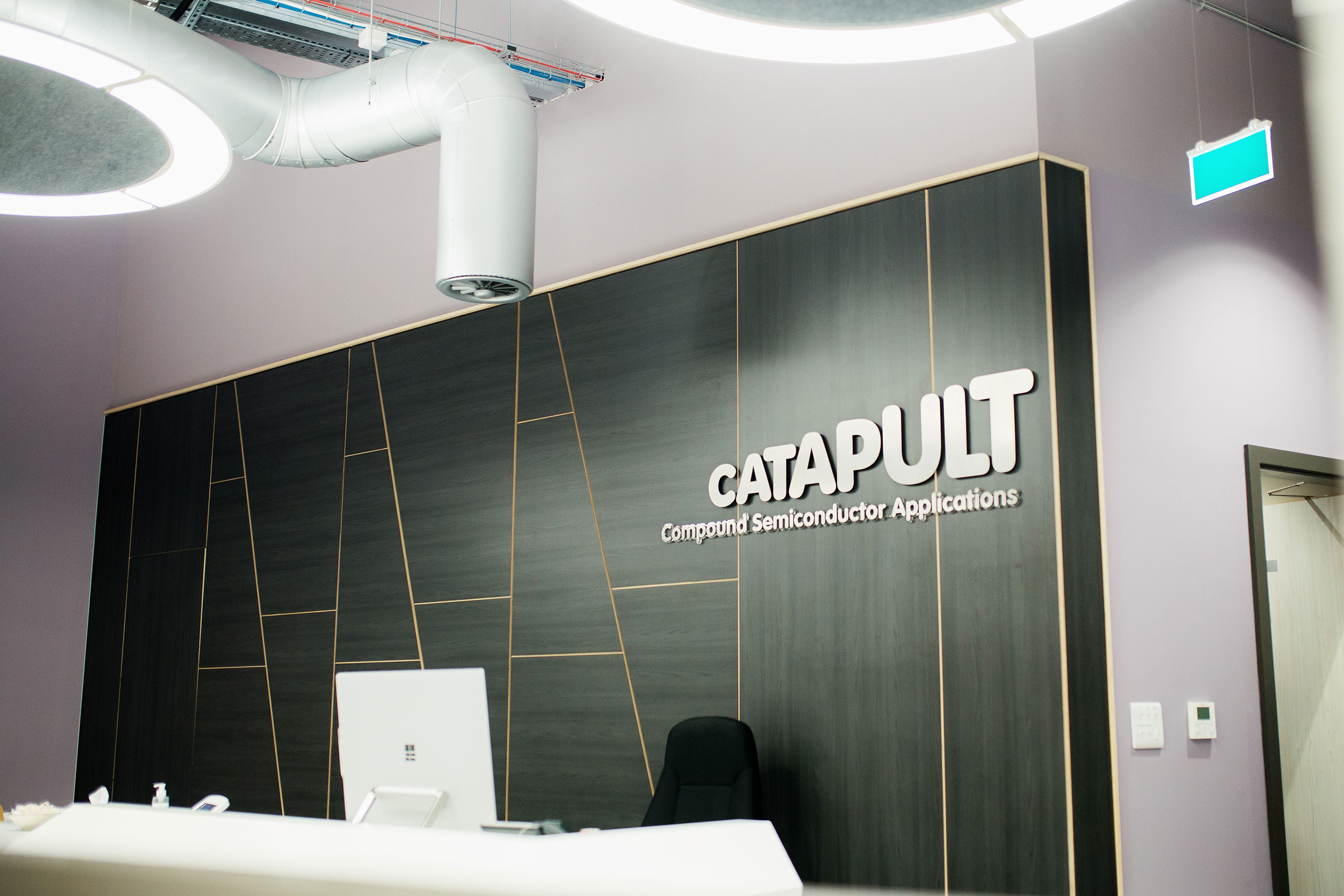 A modern office reception area featuring a sleek, dark-paneled wall with the word 
