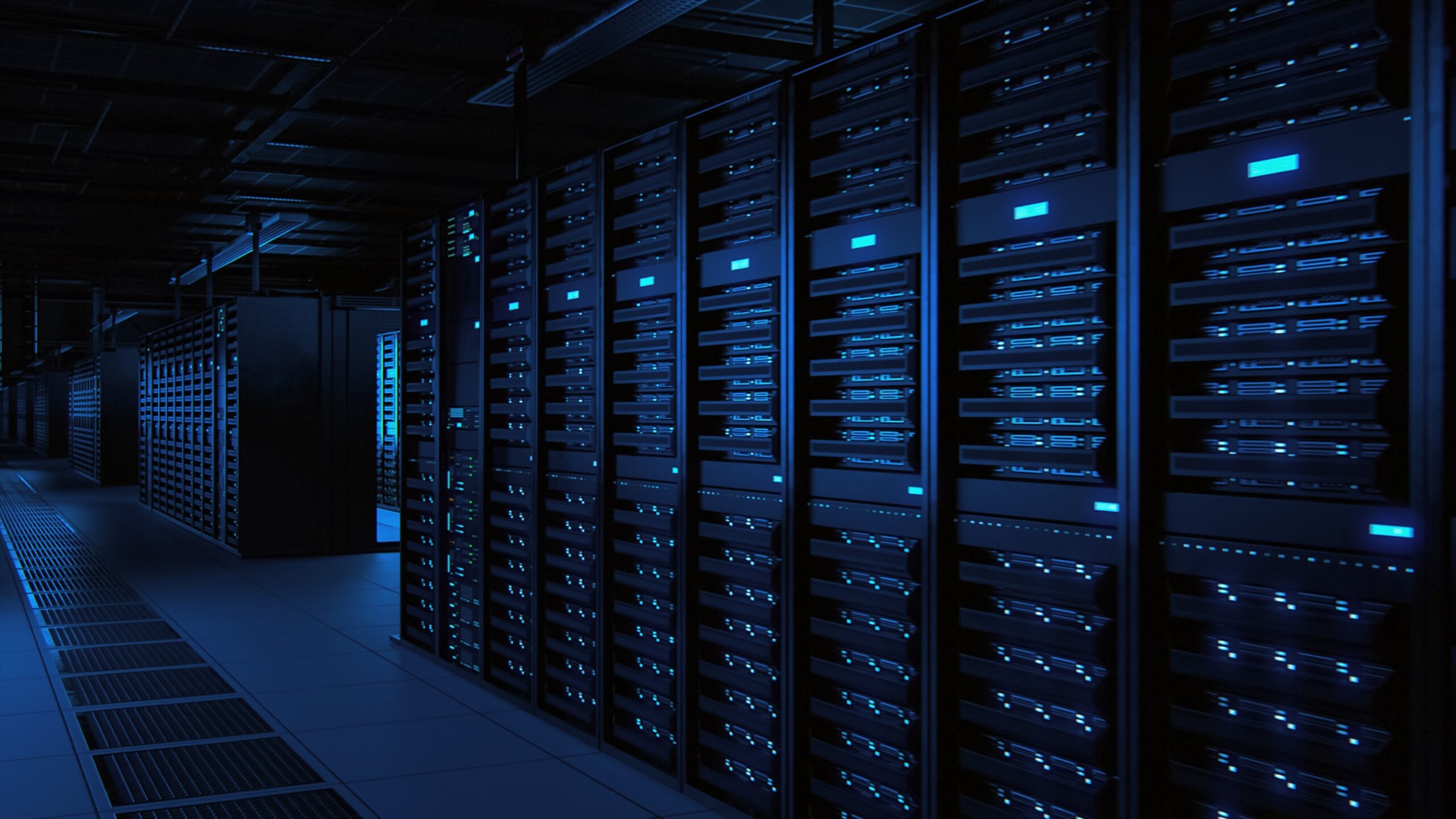 A dimly lit data center with rows of server racks illuminated by blue LED lights, extending into the distance. Each rack is filled with multiple servers, and the floor has ventilation grates. The setup gives an organized and futuristic appearance. - CSA Catapult
