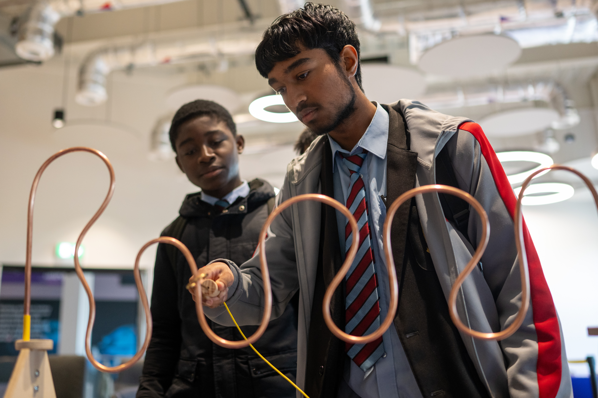 Two young men skillfully employ a tool on a copper wire sculpture in a brightly lit, modern room. - CSA Catapult