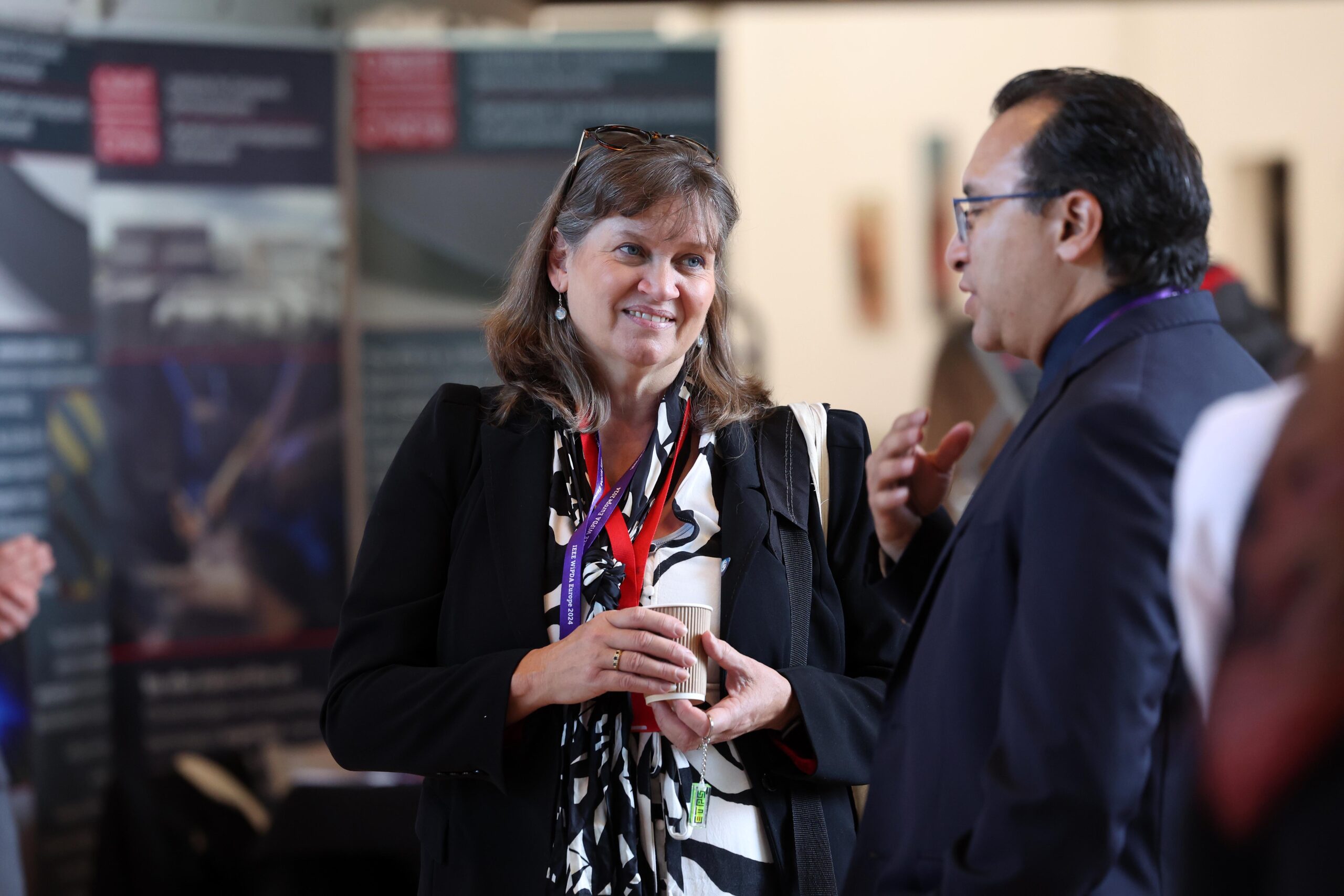 Two people engaged in conversation at an event, with informational posters in the background. - CSA Catapult