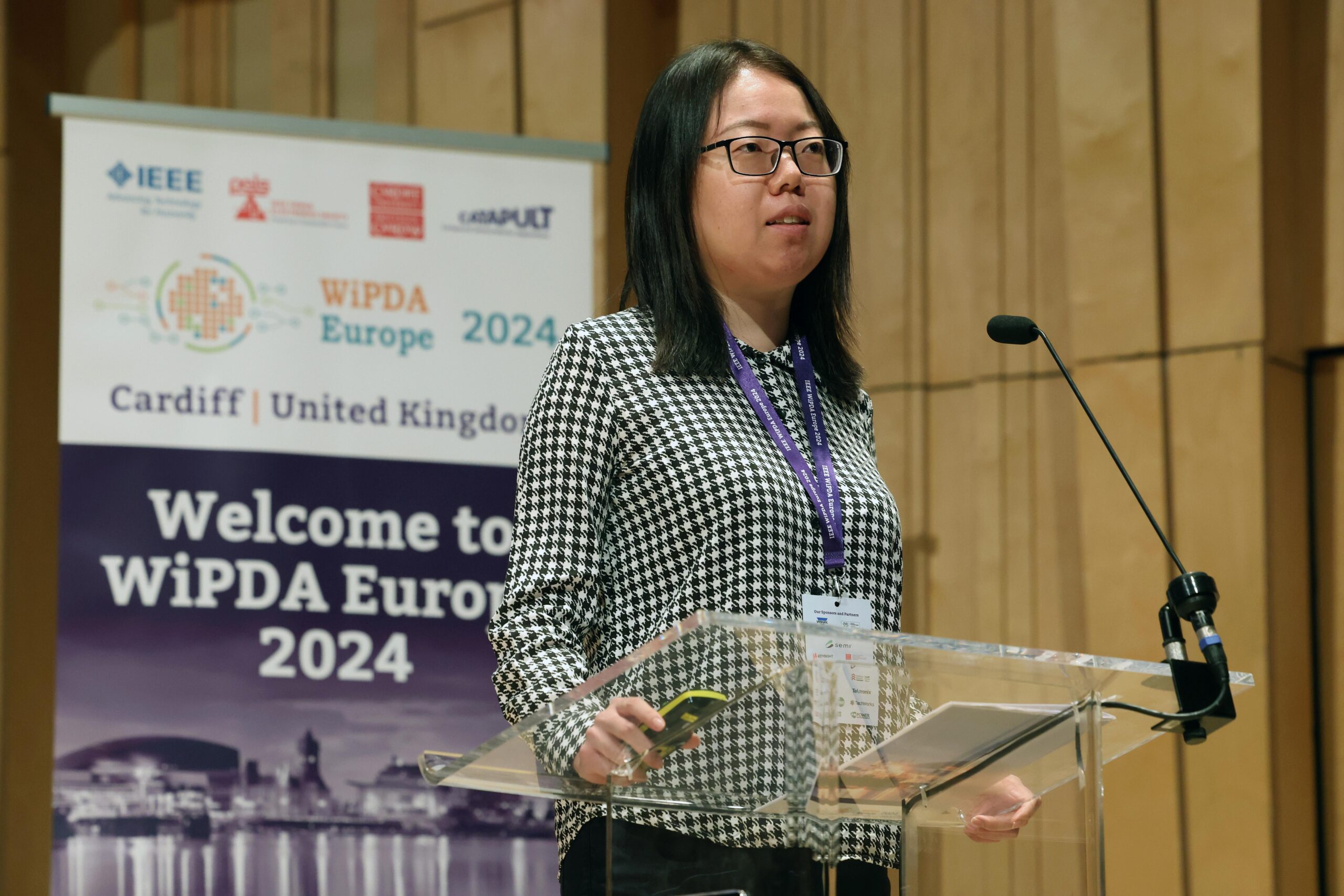 A person speaks at a podium during the WiPDA Europe 2024 event in Cardiff, UK. Banners and microphone are visible. - CSA Catapult