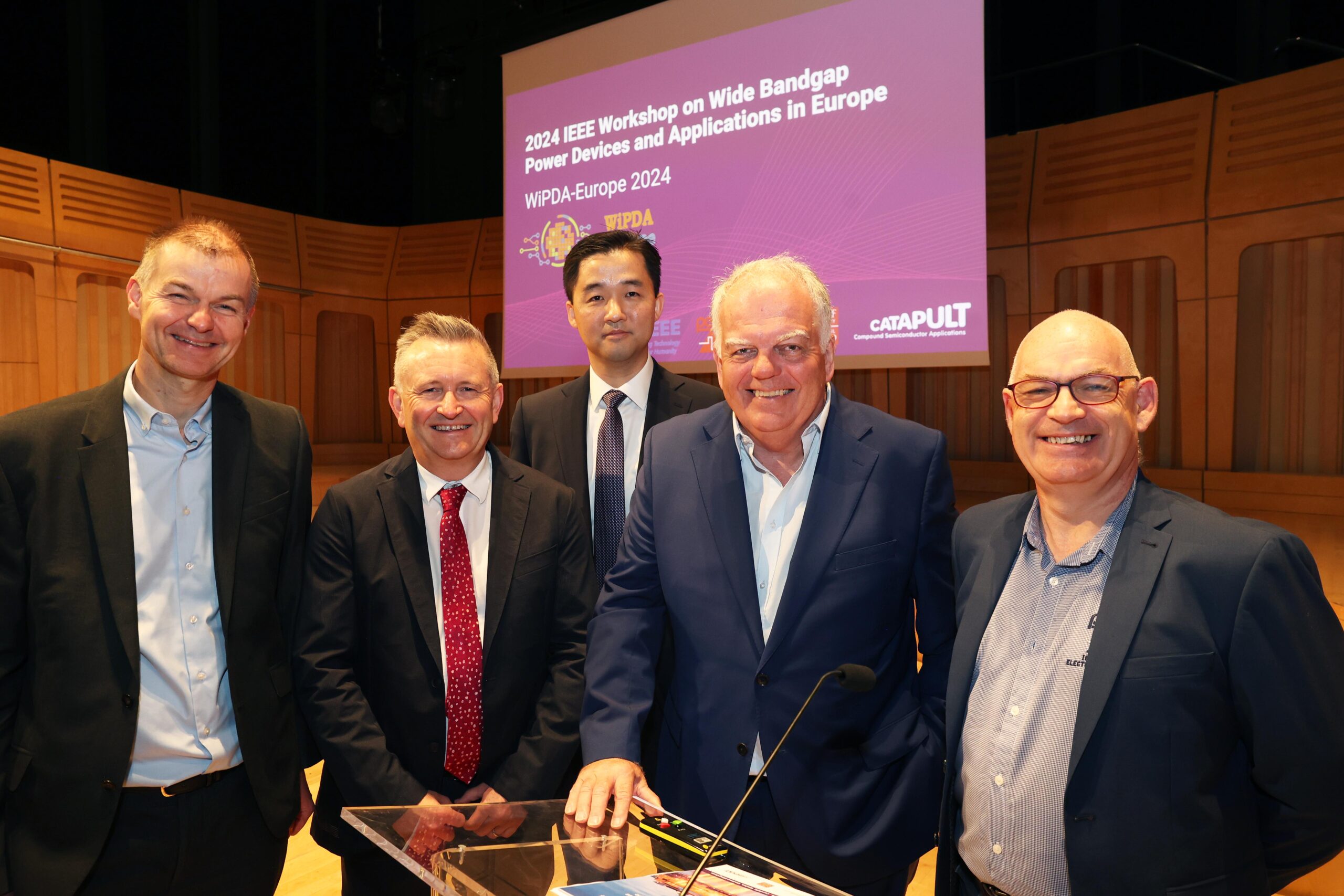 Five men in suits stand together on a stage at the IEEE Workshop on Wide Bandgap Power Devices and Applications in Europe. - CSA Catapult