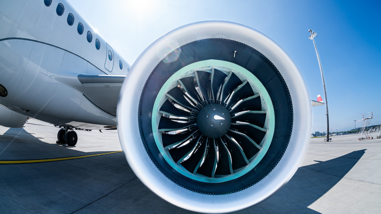 Close-up view of a jet engine on an aircraft wing, parked on an airport tarmac under a clear blue sky. - CSA Catapult