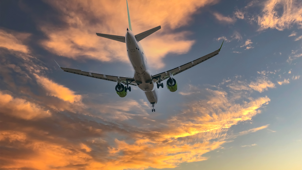 Airplane flying at sunset with a vibrant sky full of clouds seen from below. - CSA Catapult
