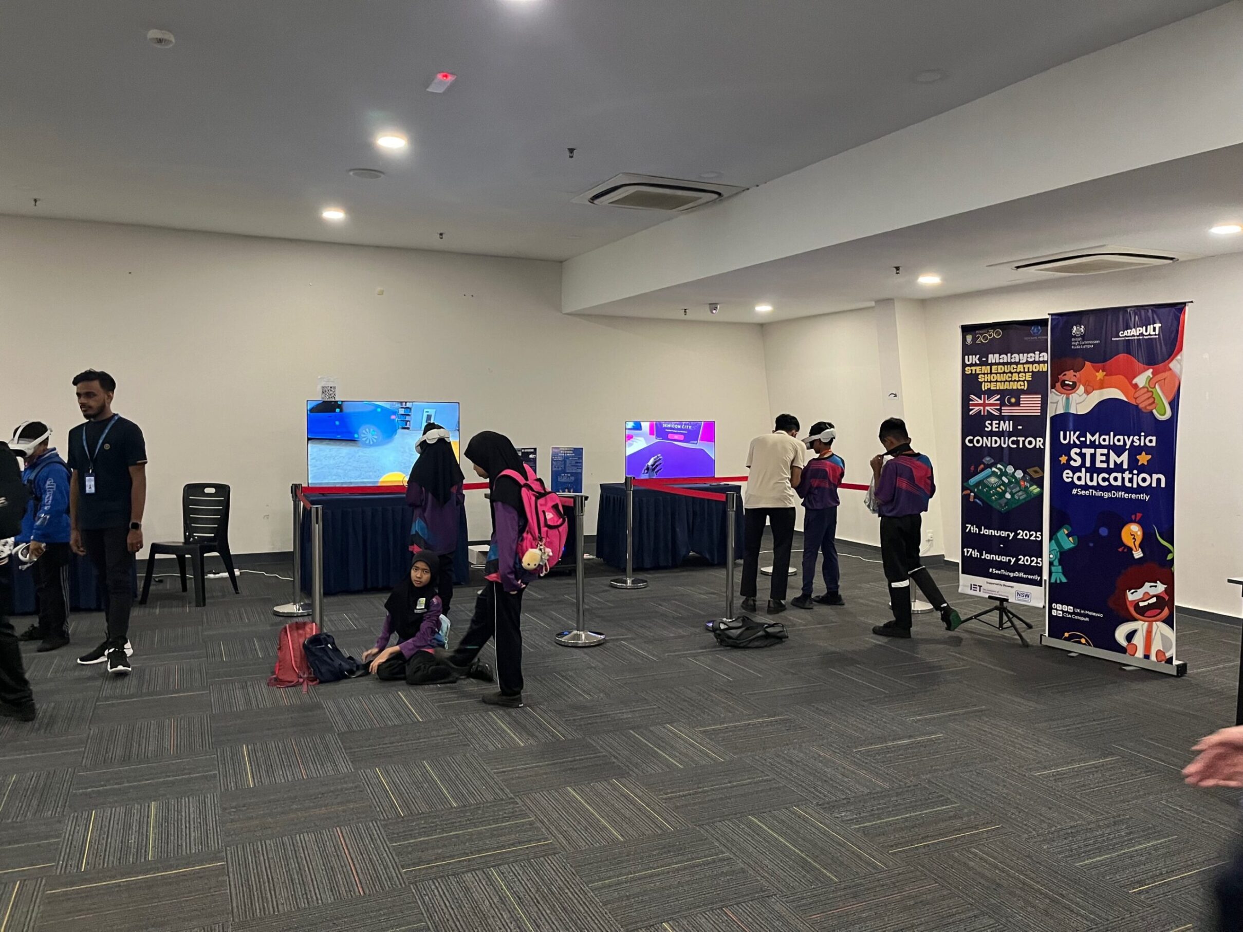 Attendees at an e-STEM event engage with banners and digital displays, some standing while others relax on the floor. - CSA Catapult