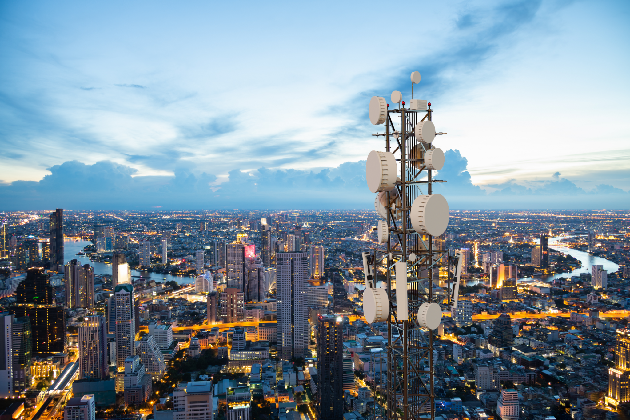 5G telecommunication tower overlooking a cityscape at dusk, with buildings and a river visible under a partially cloudy sky. - CSA Catapult
