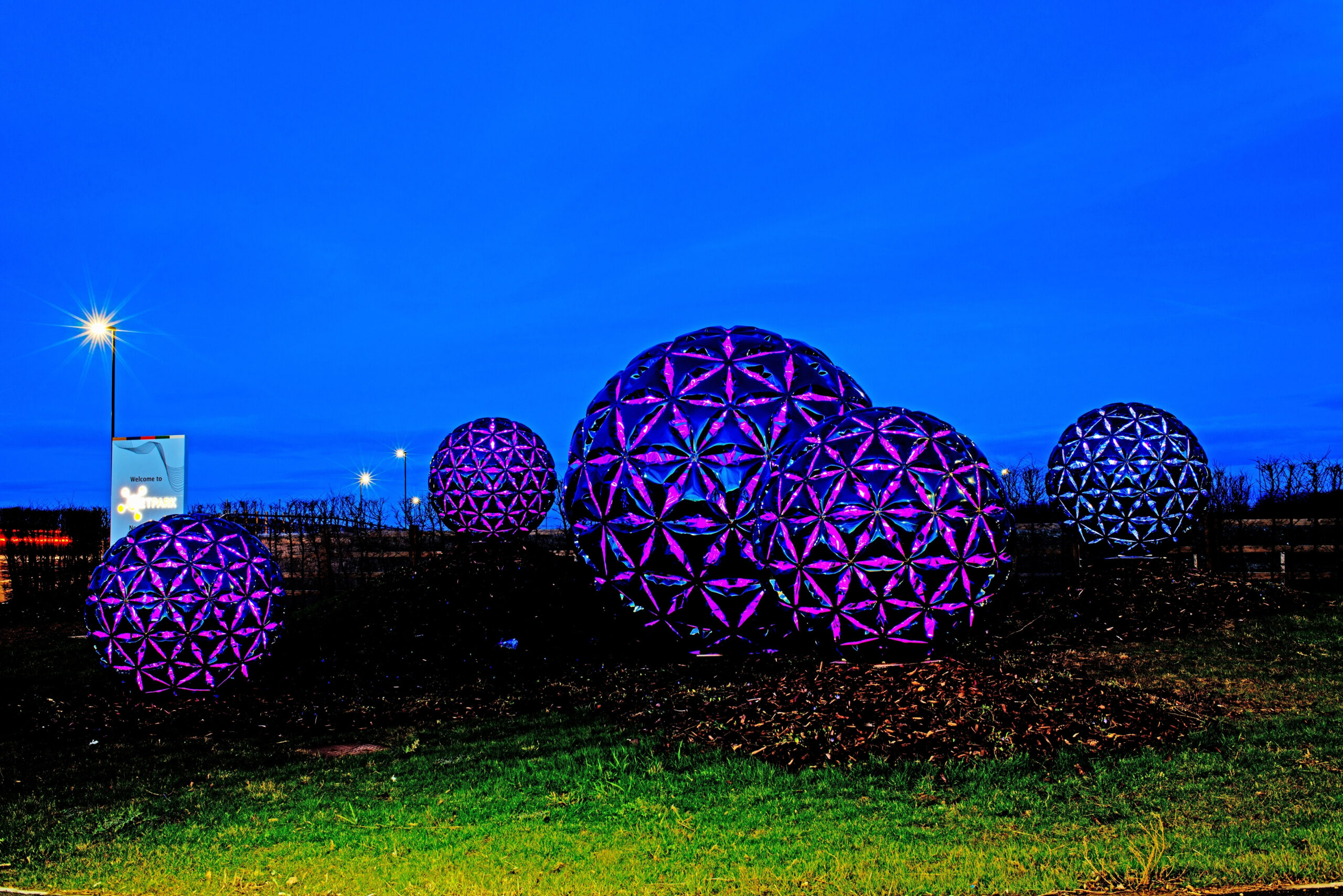 Purple geodesic spheres glow in NETPark Sedgefield against a blue evening sky, near a lit street lamp on the green. - CSA Catapult