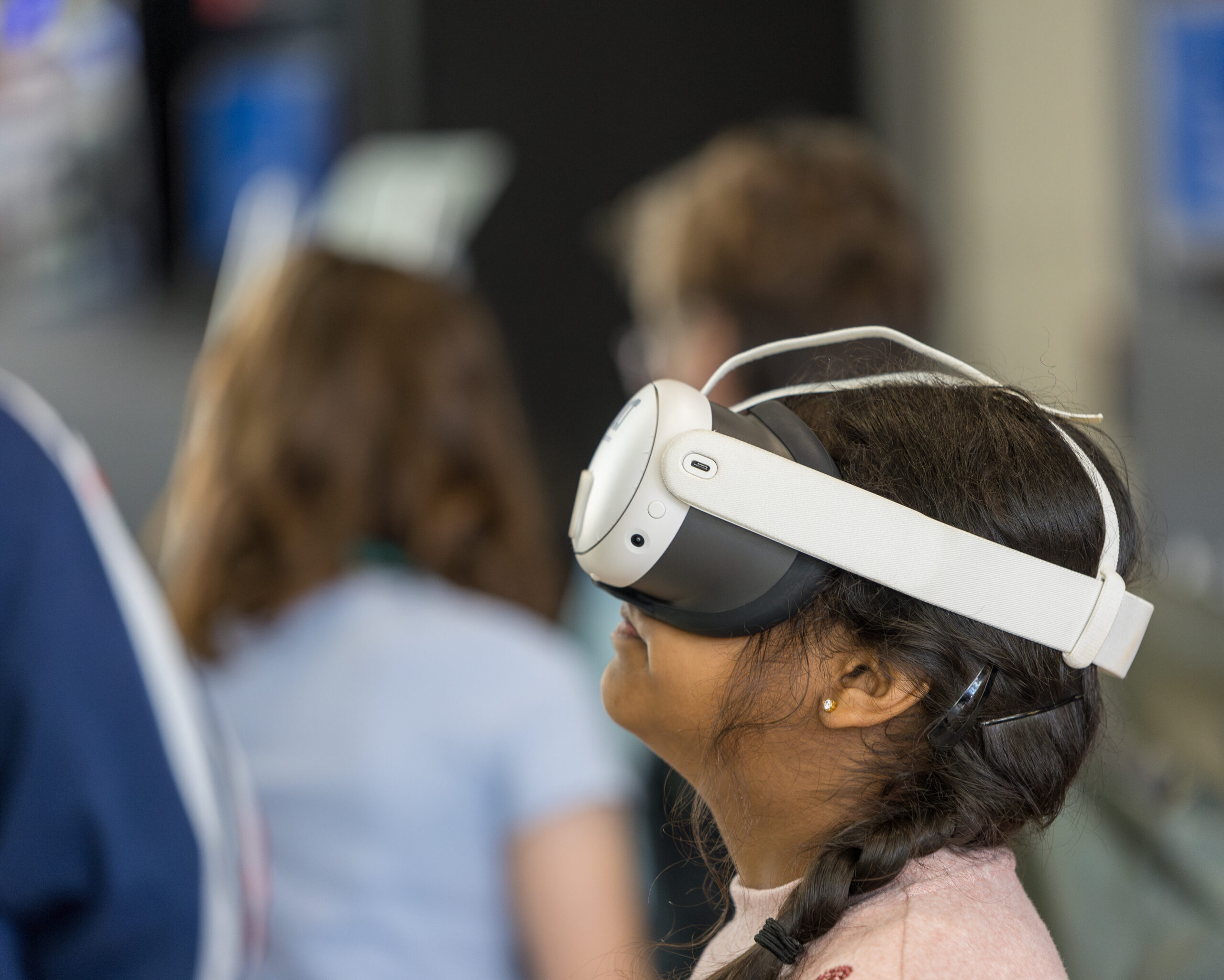 A girl with braided hair wears a VR headset at Cardiff Science Festival 2025, facing right in a room with blurred figures. - CSA Catapult