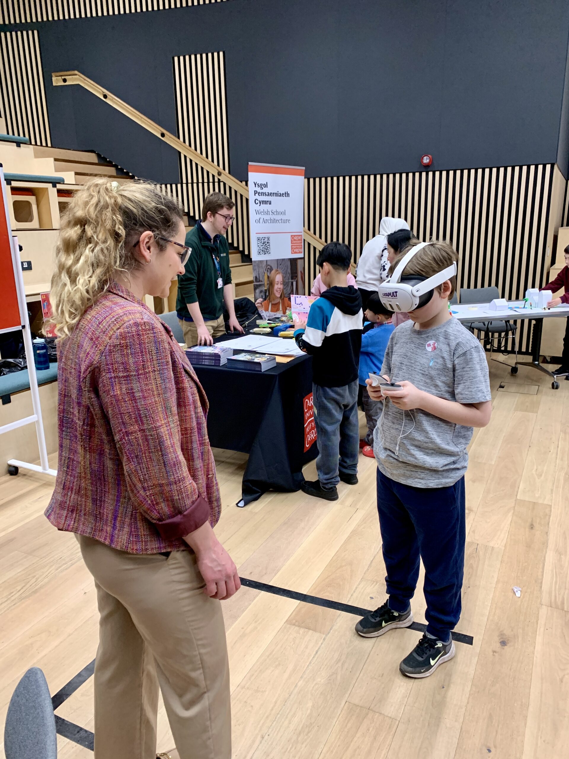 A child wearing a visor engages with a woman in a CSA classroom, while others practice skills at tables in the background. - CSA Catapult