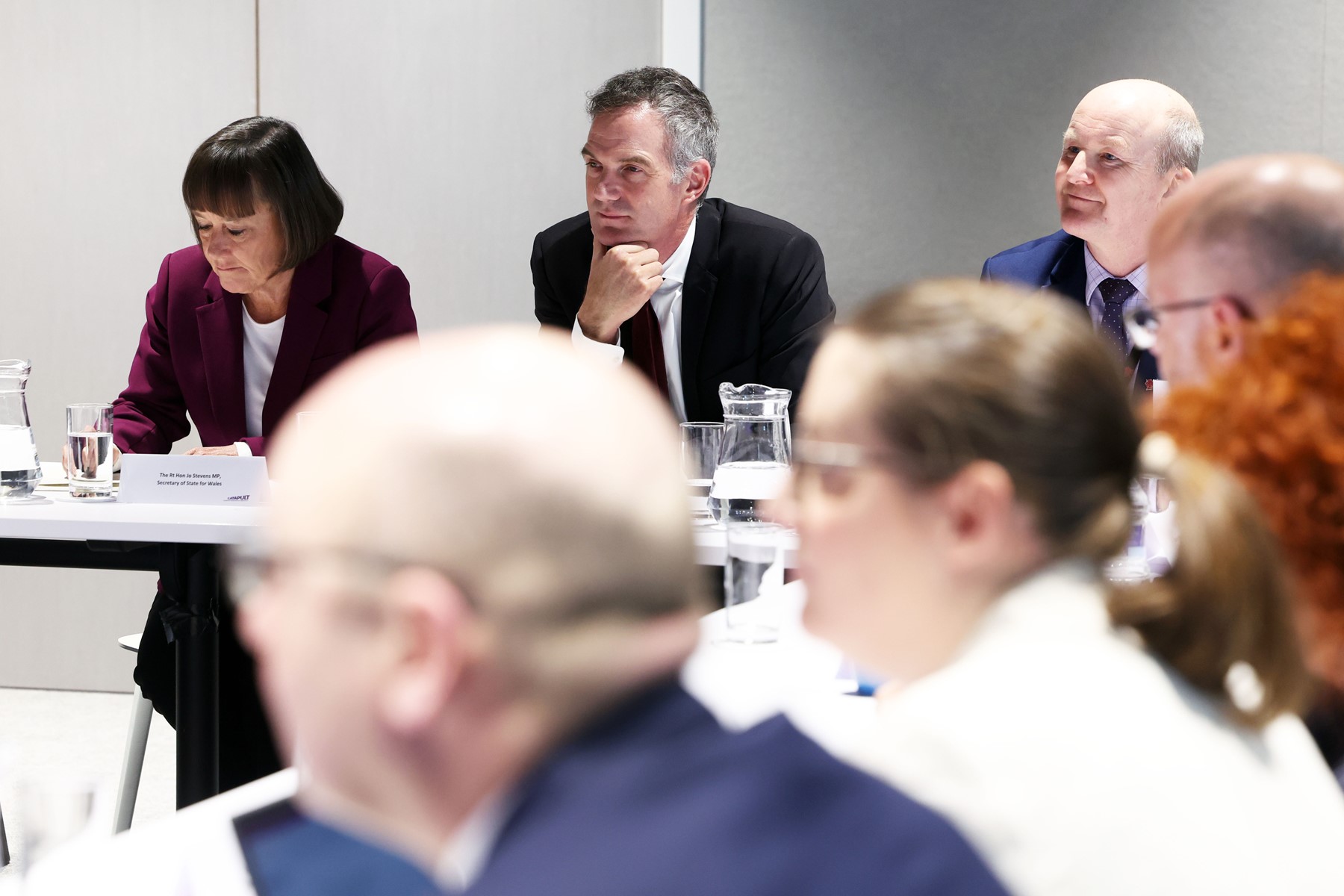 Group of people at an AME Advanced Material Electronics meeting, some taking notes, while one man listens attentively. - CSA Catapult