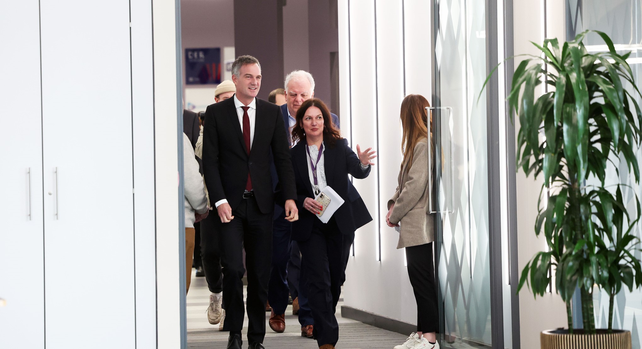 Group from AME Advanced Material Electronics walking and chatting in a modern hallway, with a large plant on the right. - CSA Catapult