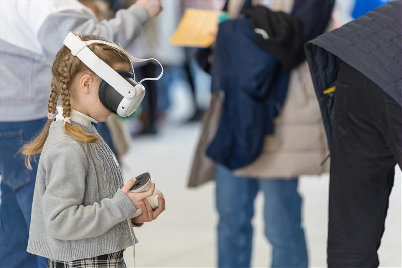 At the Cardiff Science Festival 2025, a young girl with braided hair dons a VR headset, controller in hand amidst the crowd. - CSA Catapult