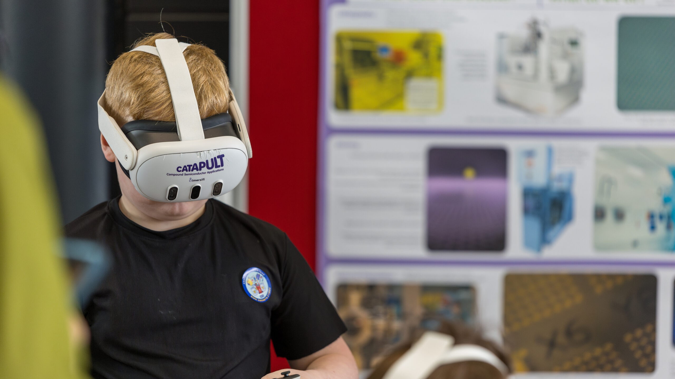 Child at Cardiff Science Festival 2025, wearing a virtual reality headset, holds a VR controller in front of an interactive display board. - CSA Catapult