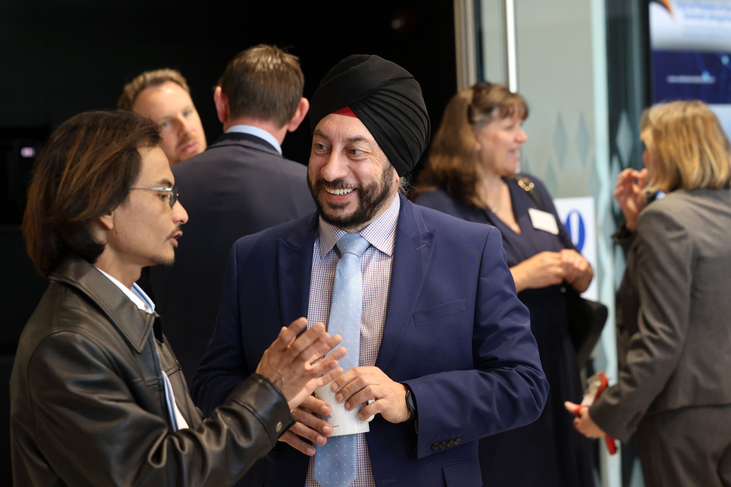 Two people in conversation at a Sarawak professional event, with others networking in the background. - CSA Catapult