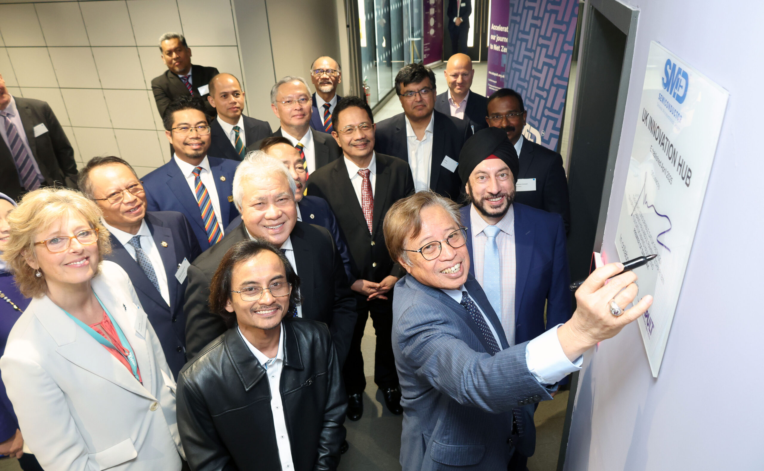 A group in business attire watch a man sign a plaque on a wall in Sarawak, all smiling for the camera. - CSA Catapult
