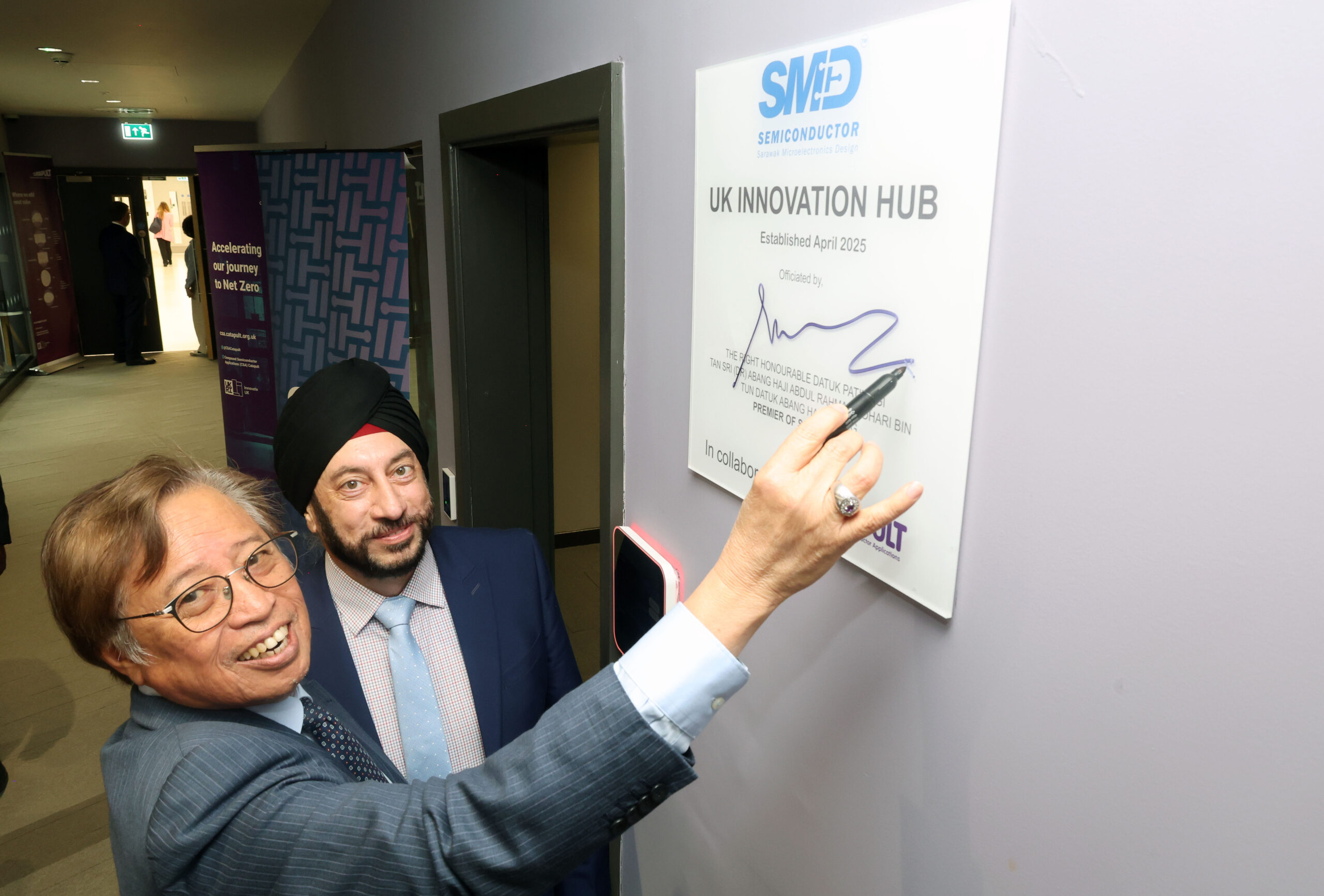 Two men smiling as The Rt Hon Premier of Sarawak signs a UK Innovation Hub plaque with CSA Catapult CEO Raj Gawera. - CSA Catapult