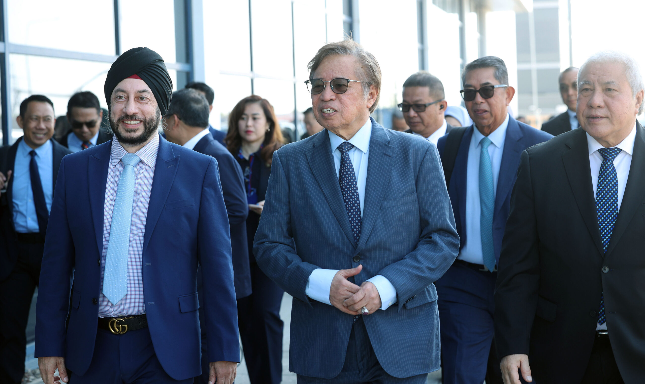 A group of men in business suits walk together outside in Sarawak, smiling and talking. - CSA Catapult