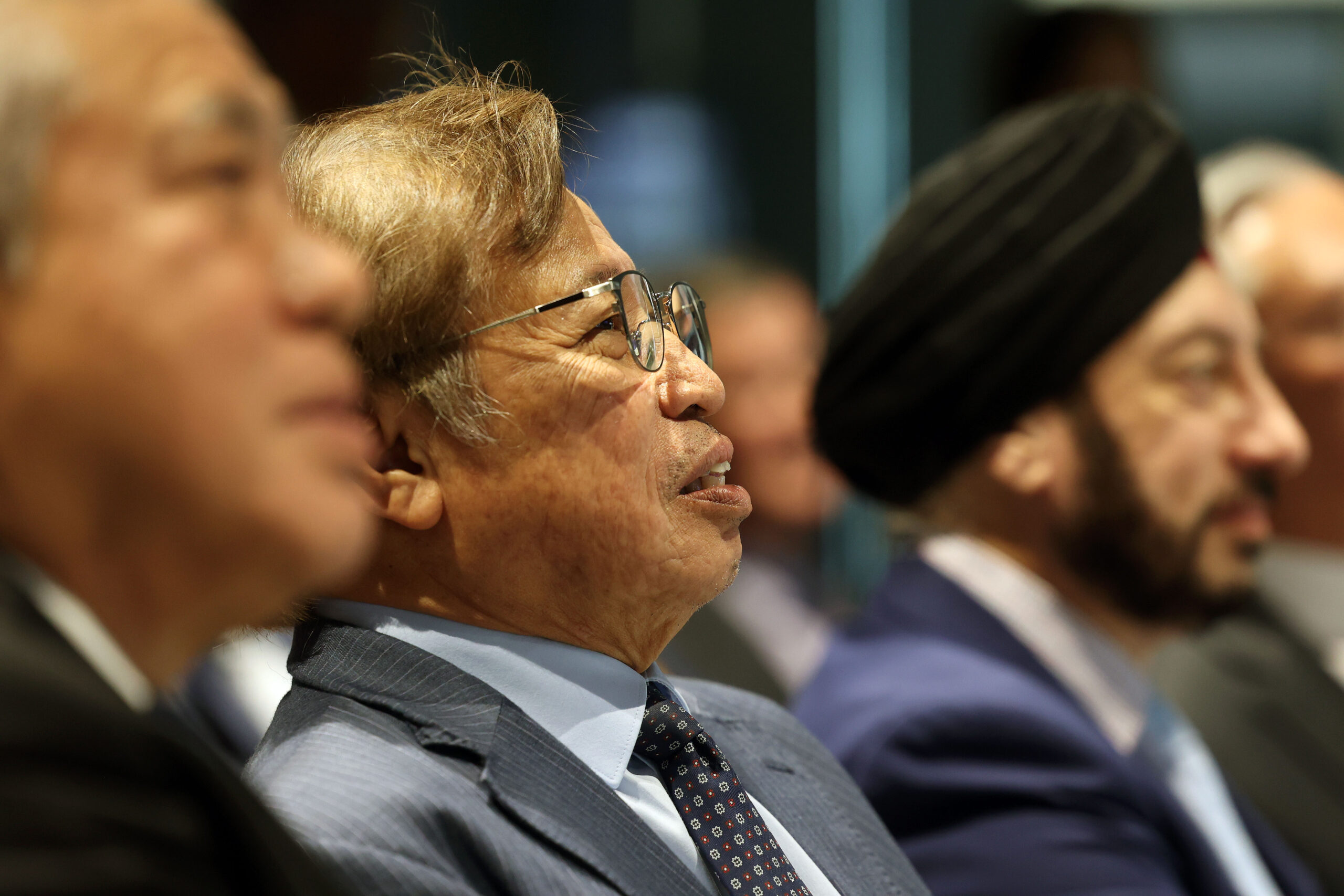 Three men in suits sit in a row, listening attentively at an indoor Sarawak event or meeting. - CSA Catapult