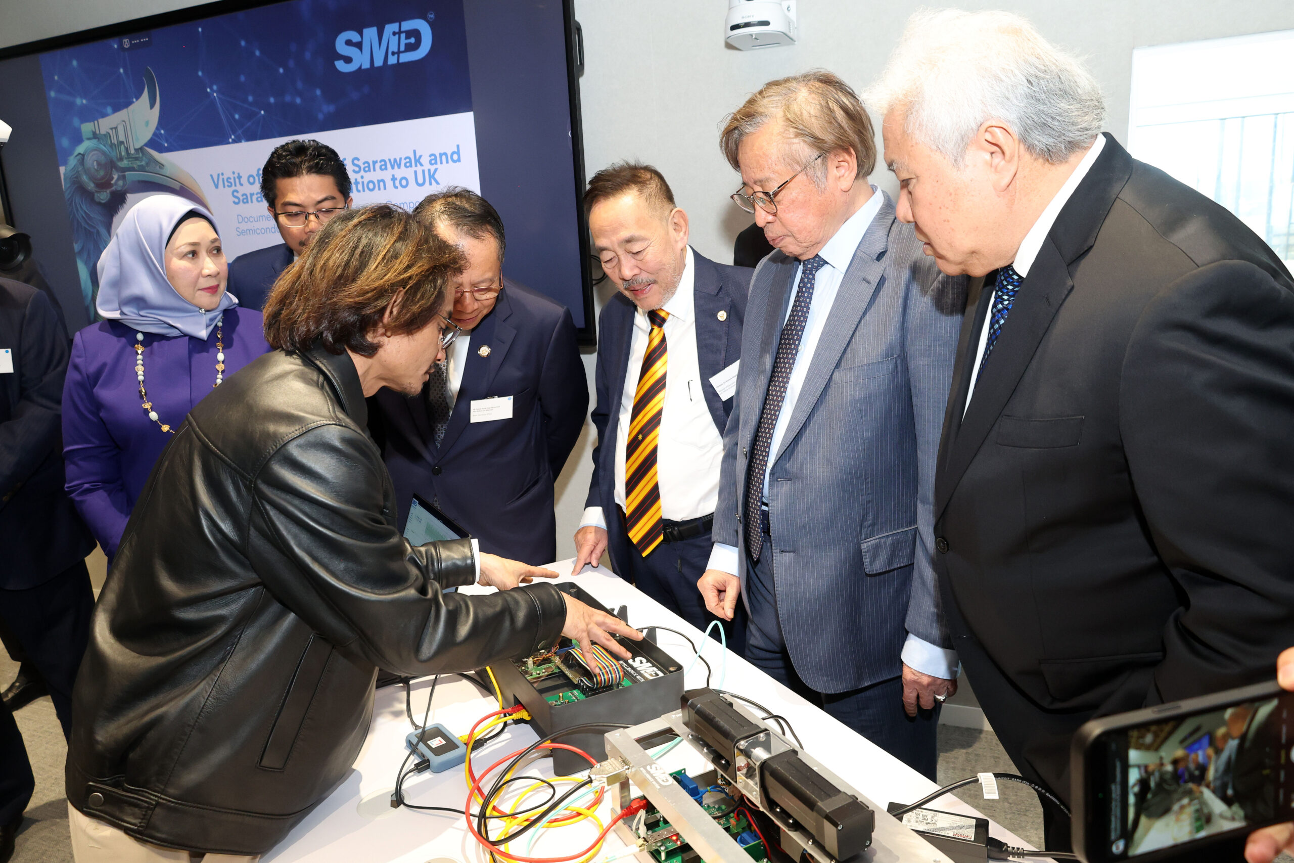 A group of people in Sarawak observe a person demonstrating electronic equipment on a table at an event. - CSA Catapult