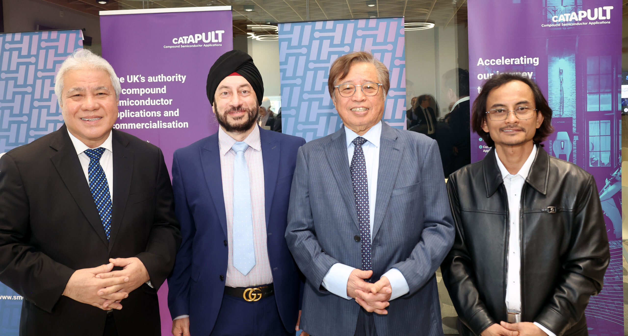 Four men in business attire stand smiling in front of purple and blue Catapult Sarawak promotional banners. - CSA Catapult