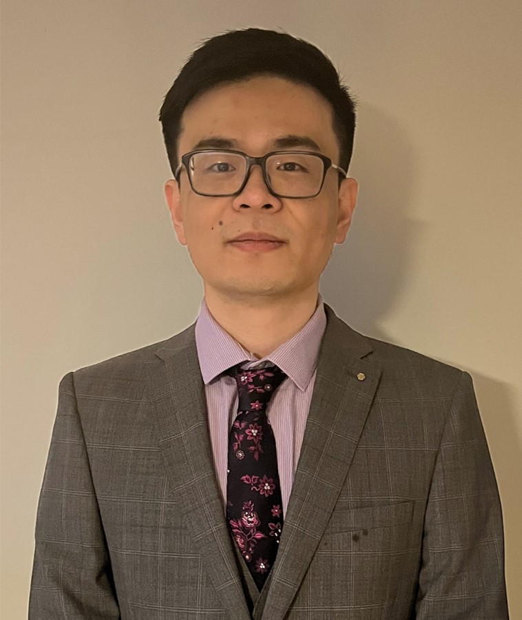 Dr Sheng Wang, lecturer at Cardiff University, wears glasses and a gray checked suit against a plain beige wall. - CSA Catapult