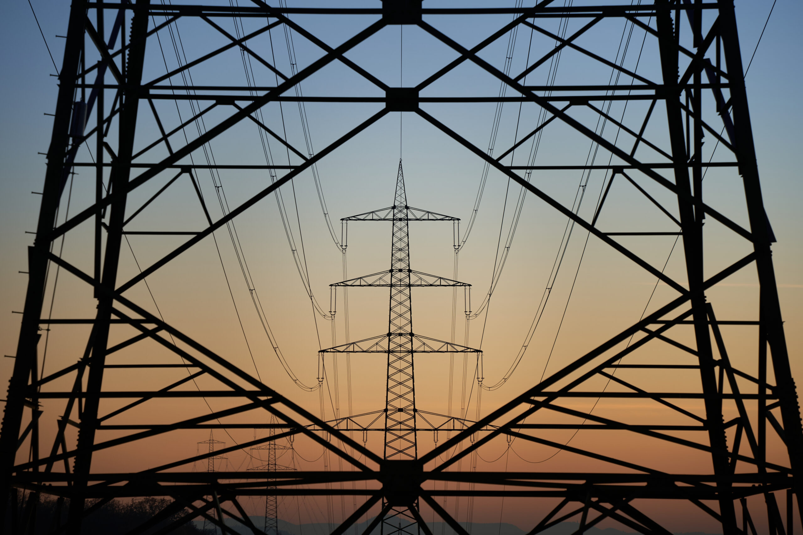 Silhouette of electricity pylons at sunset in Wales, framed by metal power lines structure. - CSA Catapult