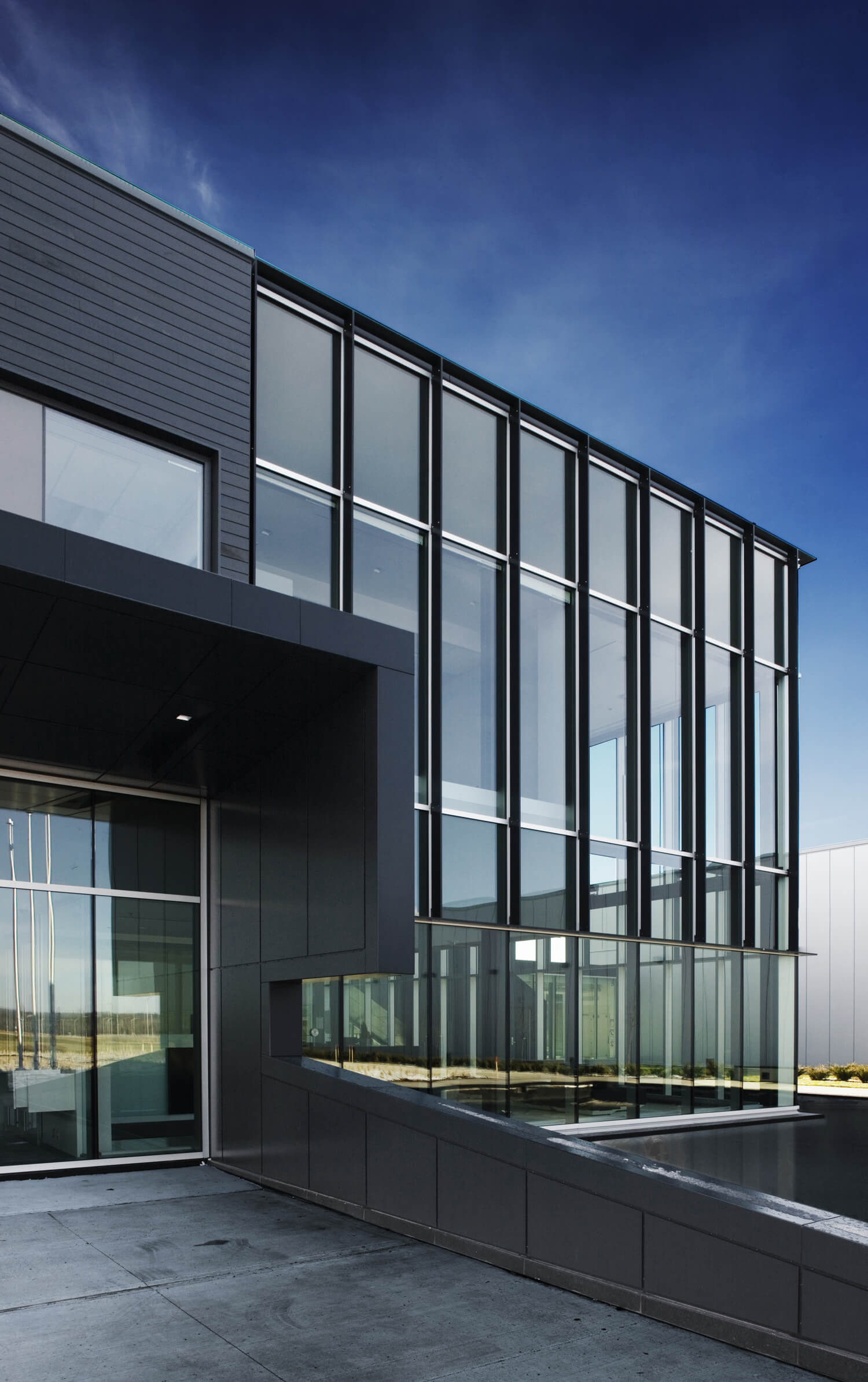 C2MI building with large glass windows, dark exterior panels, and a reflective water feature under a blue sky. - CSA Catapult