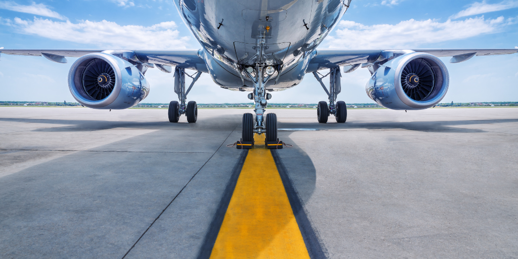 Front view of a commercial airplane on the runway, with engines, landing gear, and security measures visible under a blue sky. - CSA Catapult