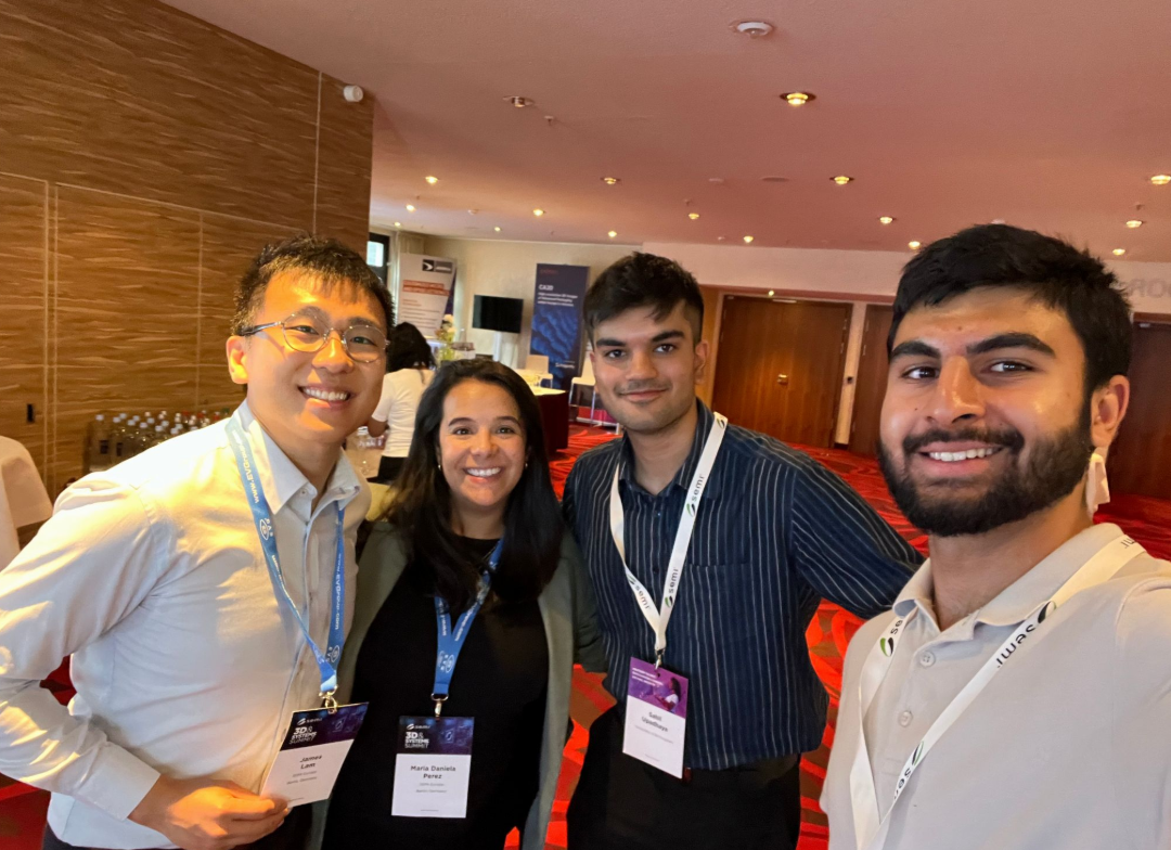 Four people wearing conference badges smile for a group selfie in a bright, modern e-conference venue. - CSA Catapult
