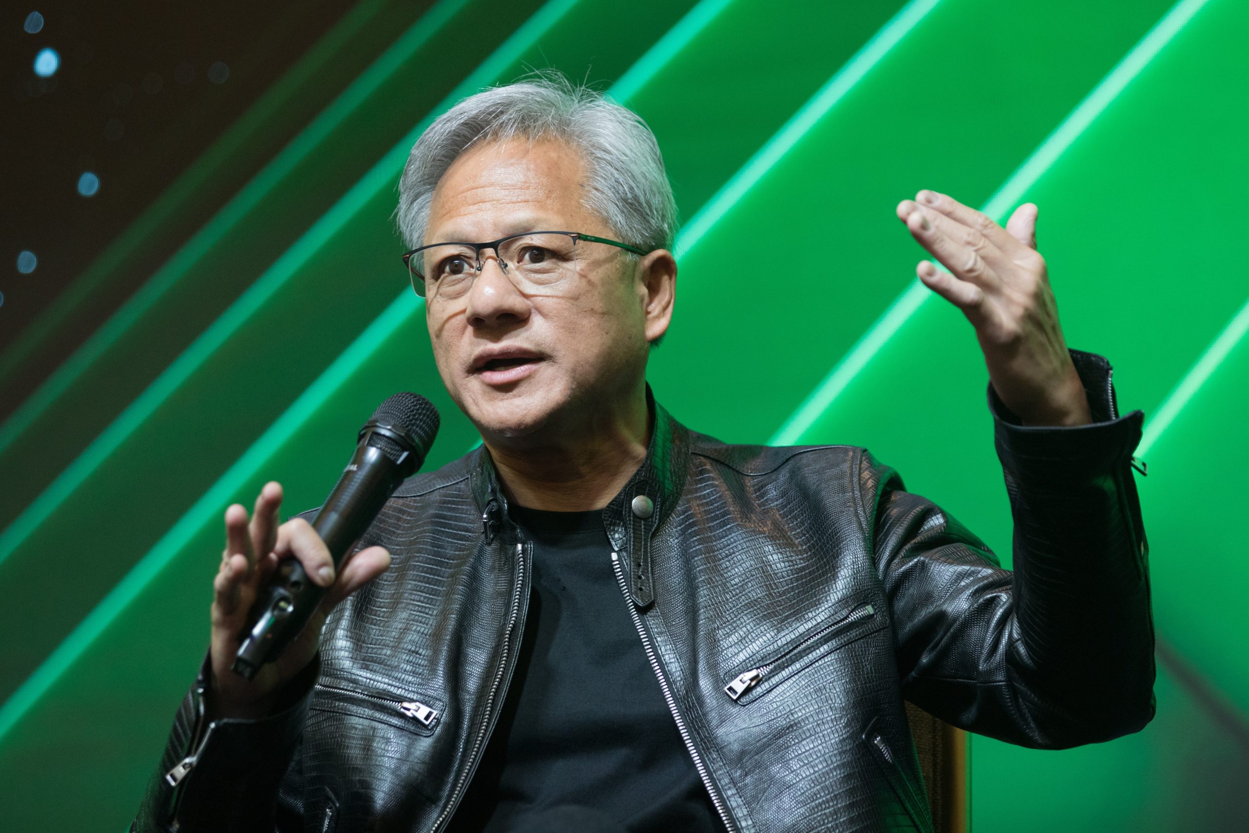 Man in a black leather jacket discusses AI into a microphone, gesturing with his hand, against a green background. - CSA Catapult
