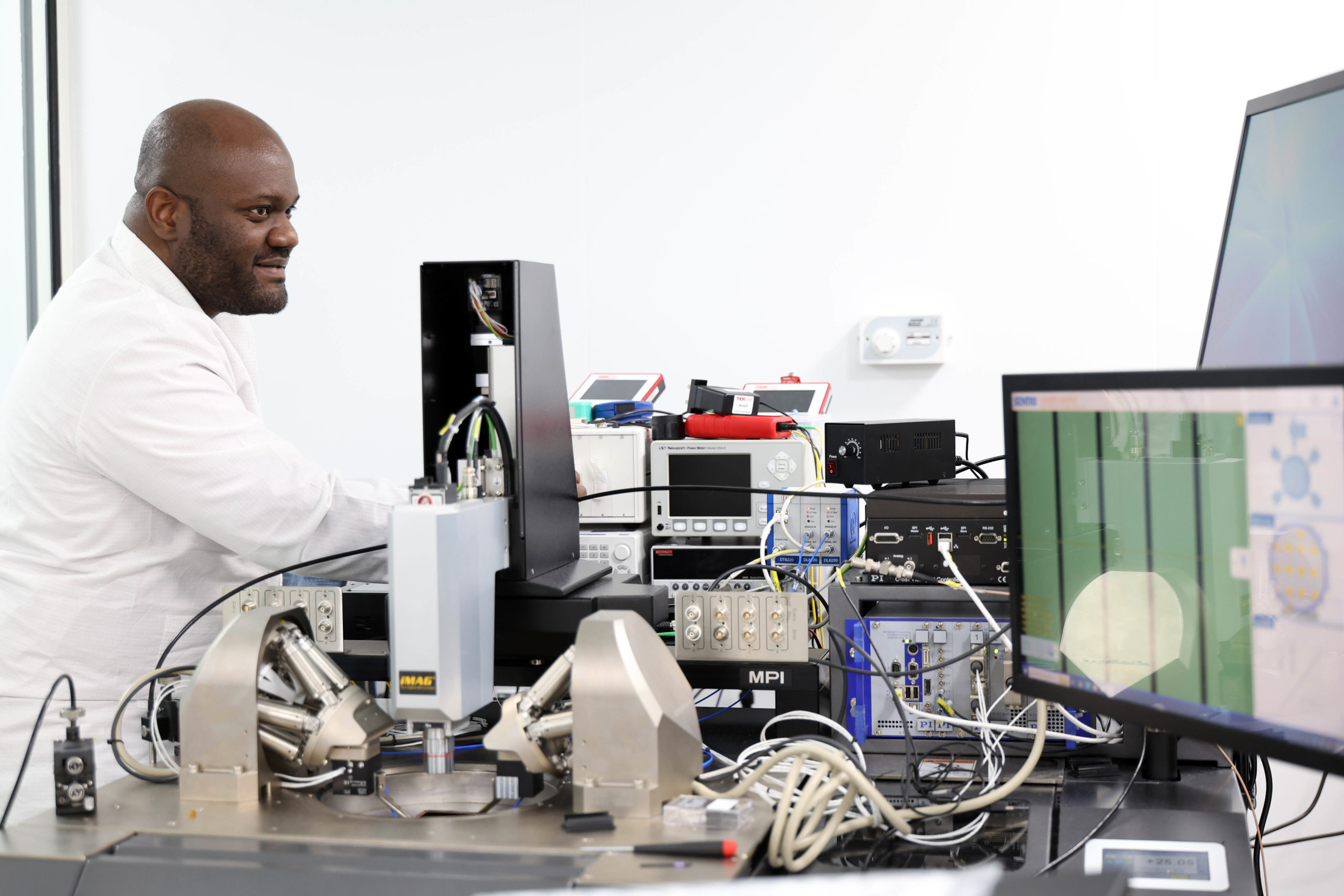 A scientist in a lab coat operates advanced scientific equipment and monitors data on multiple screens. - CSA Catapult