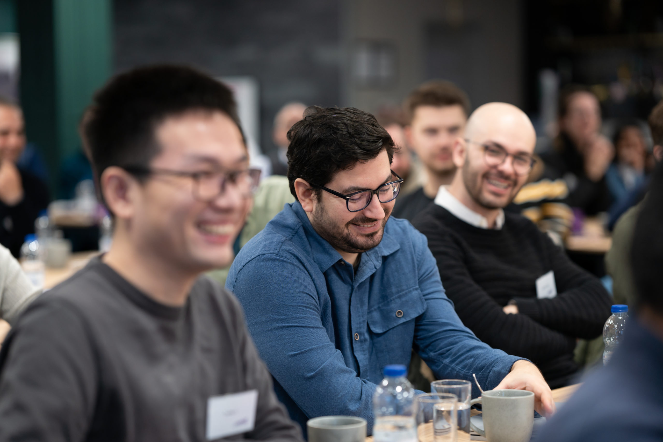 A group of people sitting at tables, smiling and listening during an indoor event or meeting. - CSA Catapult