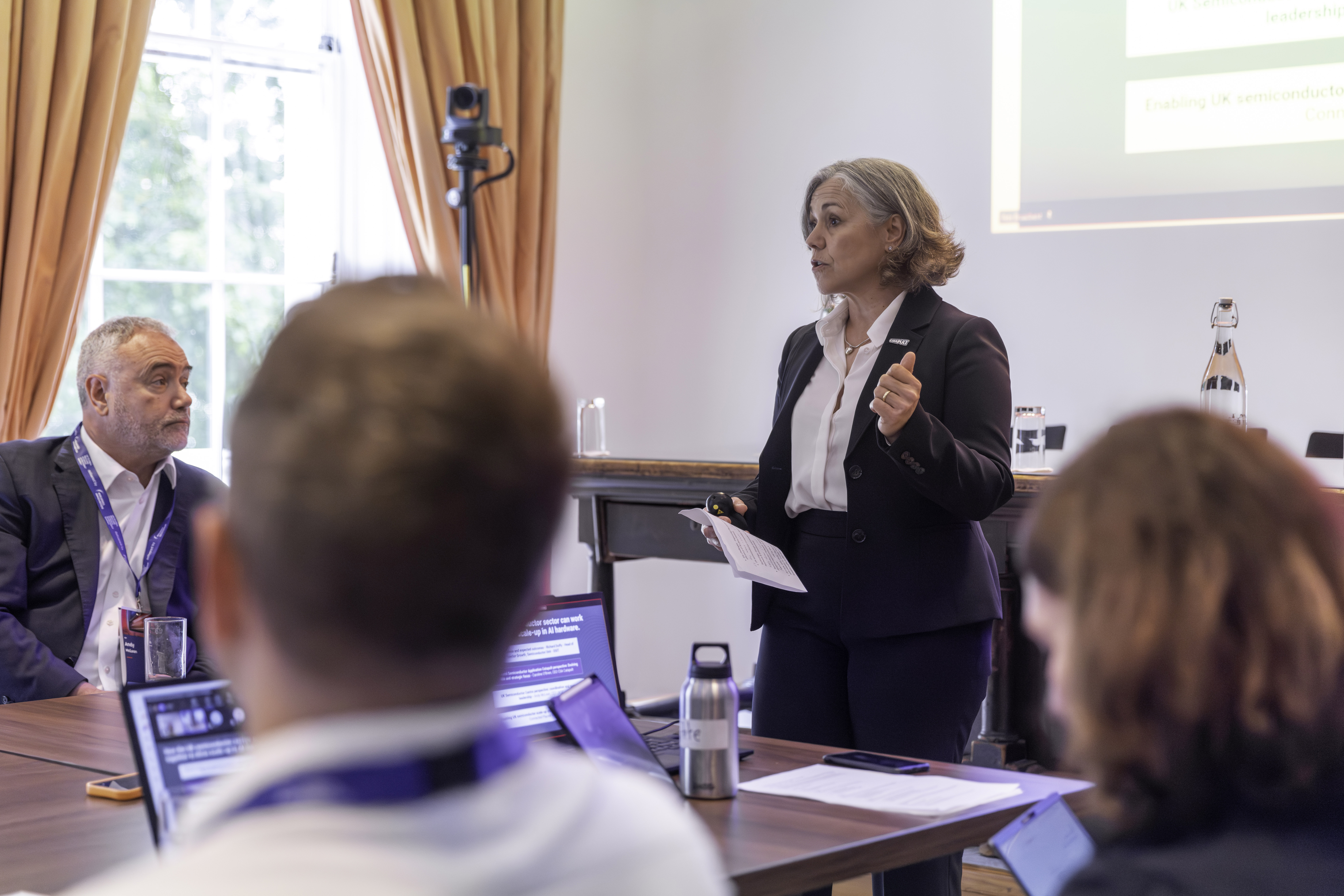 A woman gives a presentation to a group in a meeting room with laptops and a large window. - CSA Catapult